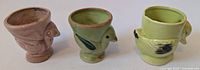 Three chick-shaped ceramic egg cups photographed from the front, showing distinct colors and shapes.