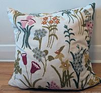 Front view of large square pillow with colorful woolen floral embroidery on heavy cotton fabric, showing pink, blue, yellow, and purple flowers on white background.
