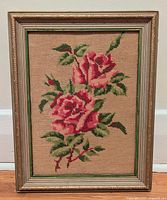 Full view of framed rose needlepoint showing two pink roses and foliage with gold-tone frame.