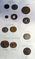 Coins from India, China, Egypt, Oman, South Africa, and Napoleonic coin laid out on white paper with handwritten country and dates.