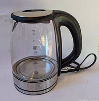 Front and side view of Salton electric glass kettle showing transparent glass body with water level markings, black handle and stainless steel base.