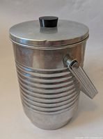 Photo of vintage aluminum ice bucket with ribbed body, circular lid with black knob, and ribbed side handle.