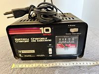 Front view of used Motomaster 10 amp battery charger showing 6V and 12V voltage selector, 10 amp label, analog charge zone meter, and power cord.
