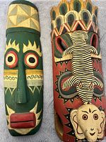 Front view of two African tribal wood masks side by side lying on fabric background, showcasing color and detail.