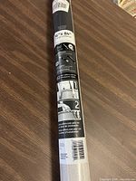 Rolled aluminum frame screen package laid on wooden table, with labels and barcode visible.