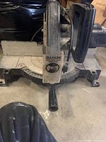 Front view of the Black and Decker power miter saw showing the handle, blade guard with safety label, and base with angle markings.
