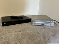Photo showing the black LG Blu-ray player with remote on top and silver ONN DVD player side by side.