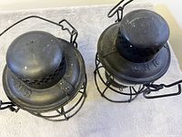 Top view of two metal oil lamps showing CNR markings on the perforated chimney tops with wire handles.