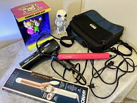 Photo showing Conair hair dryer and curling iron in box, pink NuMe straightener, Suomi soft carrying case, and novelty Polite Fight game figurine with small skeleton figure.