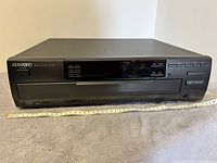 Front view of the Kenwood 5-disc CD player showing the main control panel, digital display, and disc tray.