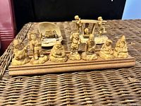 Front view of 9 mini Japanese god figurines displayed on a wooden stand, showing detailed poses and facial features of each tiny figure.