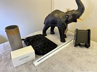 Photo shows two wireless speakers, a black charger stand, a black textured pouch, a carved elephant figurine with tusks and raised trunk, and a white ruler for scale.