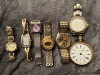 Full view of all 7 vintage watches laid out on gray textured fabric.