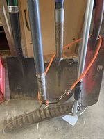 Four gardening tools, including two shovels, a rake, and a small weeding tool, all visibly used with dirt and wear