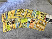Spread of approximately 60-70 used Pokemon cards with yellow borders showing various Pokemon characters and moves.