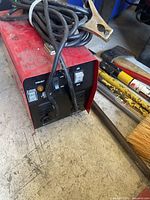 Power Fist arc welder front panel with power switch and heat level toggle switch shown, cables and clamps placed on top, machine on concrete floor with nearby tools.