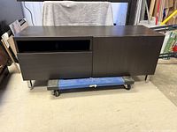 Single image showing one TV stand with dark wood finish, open shelf, drawer, and cabinet door. The stand rests on metal angled legs.