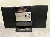 Front view of Sony CMT-FX300i stereo system with two speakers, showing display, controls, and iPod dock.