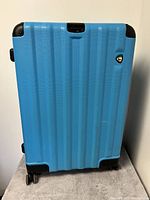 Front view of bright blue textured hard-shell suitcase with Mio Toro Ructa logo.