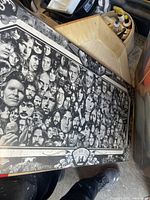 Photo of the large black and white poster board showing a collage of faces, laid on the floor with surrounding clutter.
