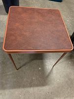 Front view of the square brown textured card table with folding metal legs showing the condition and design.