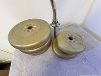 Weight lifting bar and stack of 10lb and 5lb weight plates on towel.