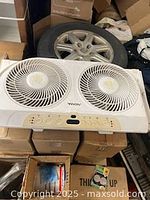 Front and top view of white Vornado window fan showing two circular fans and control panel for settings.