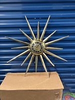 Full view of vintage starburst style wall clock with metallic spokes and central dial, showing overall shape and size.