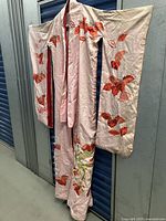 Full view of vintage silk kimono hanging, showing length and overall design with red and orange embroidered leaves on pale pink silk fabric.