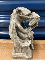 Side view of cast cement gargoyle statue reading a book, showing wing and figure details