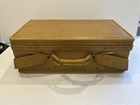 Front view of closed brown textured leather suitcase with leather handle and side straps.