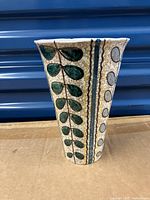 Front view of the ceramic vase showing the vertical leaf and abstract dot patterns in green, blue, white, and yellow.