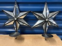 Pair of star-shaped mirror sconces with candle holders in metal frame showing front and angled mirrored panels, blue door background, cardboard underneath.