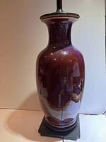 Full view of the lamp showing its vase shape and deep red glaze with reflections and lamp fittings on top.