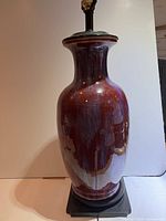 Full view of sang de boeuf glaze Chinese porcelain lamp on dark base with tall vase shape.