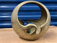 Front view of the solid brass swan planter showing the swan's head and detailed feather engravings with circular planter shape.