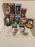 Lot of new and used baseball figures including boxed Sports Illustrated Pewter Figures, Headliners XL bobbleheads, and loose plastic and McFarlane baseball figurines arranged on white table.