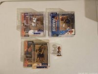 Lot of four basketball figures including three McFarlane NBA figures Mike Bibby, Steve Francis, Dwight Howard in original packaging, plus one smaller Reggie Miller figure outside packaging on white table surface.