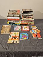 Photo showing most of the books stacked in two piles with some laid flat in front providing details on titles and condition.