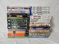 Photo showing stacked DVDs including Modern Family, Boy Meets World, The Office, Madam Secretary, Your Honor, CSI seasons 1-3, House seasons 1-4, and Big Bang Theory Blu-Rays.