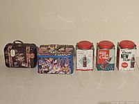 Five collectible tins arranged in a row on a white surface including 3 Coca-Cola tins, 1 Disney tin, and 1 Girl Scouts tin.