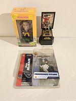 Photo of three football figures: McFarlane Steve McNair figure in plastic blister pack, Headliners XL football player figure in yellow box, Joe Montana statue on stand with framed card