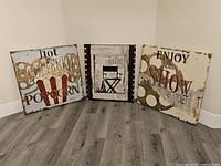 Three canvas art pieces arranged on floor against wall, showing full set and themes