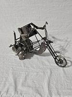 Angled view of metal motorcycle wine bottle holder showing the seat, handlebars, and front wheel detail.