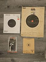 Photo showing all items laid out including Tasco Scope Guide in package and three different paper targets of various sizes and distances.