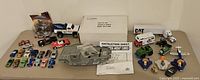 Wide view of all assorted toy cars, trucks, aircraft, and box of Sears Micro Action Aircraft Carrier with instruction sheet.