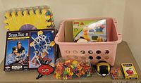 Photo of boxed Steel Tec Ferris wheel set, multicolor foam floor tiles stacked, a pink basket containing Lego Duplo box and plush toys, bag of magnetic letters and numbers, tape measure, and alphabet flashcards.