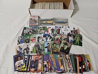 Two white boxes with trading cards lined up inside and some cards spread around showing various NASCAR and Monster Truck driver designs and automobile images.