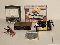 Photo showing all items together including analog meter, FM cordless room monitor box, multi-way switch box, magnetic eraser, cables and power adapter.