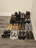 Photo showing 18 pairs of women's shoes arranged in rows on floor, including boots, sneakers, flats, sandals, and heels in various colors and styles